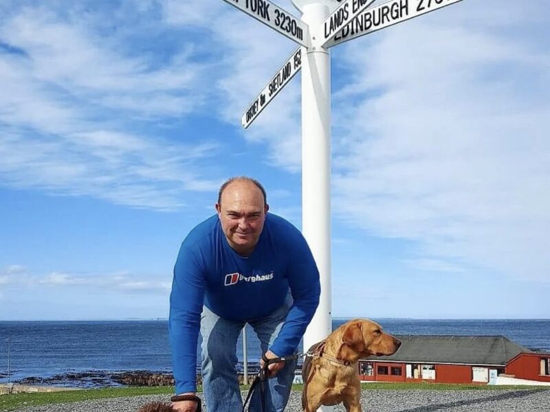 Man with a Lagotto Romagnolo and a Labrador at the John O'Groats landmark.