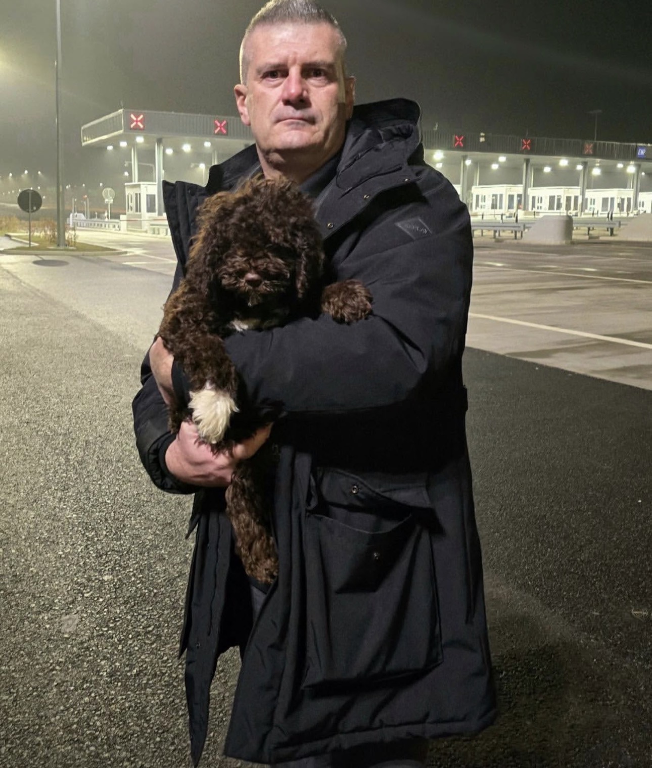 New owner picking up his brown and white Lagotto Romagnolo puppy at night.