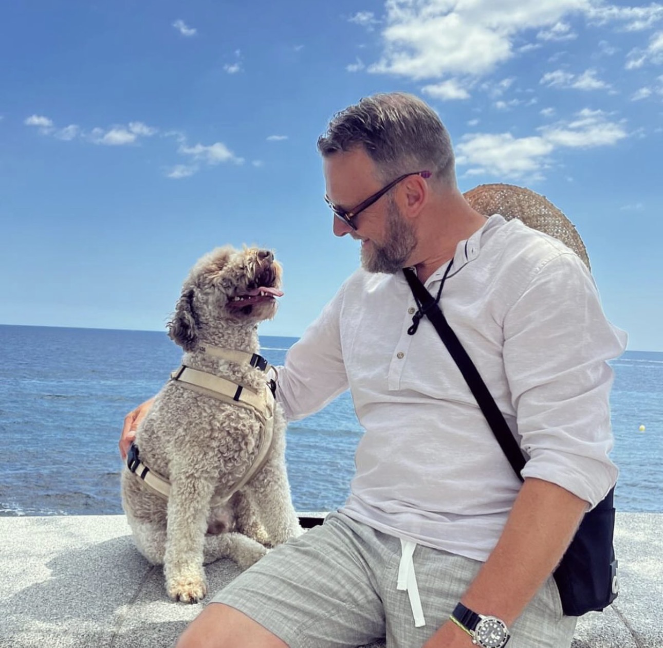 Man and his Lagotto Romagnolo sitting by the blue ocean.
